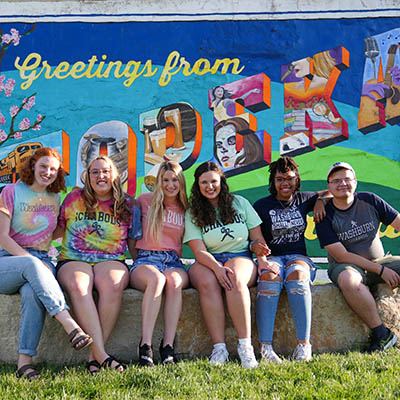 Students smile in front of a Topeka mural