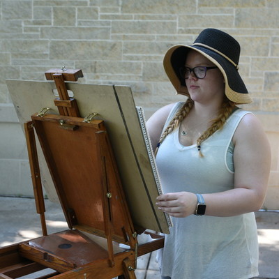 Student drawing on easel outside on campus