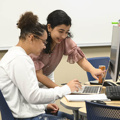 Two students smile while working on math homework in a computer lab.