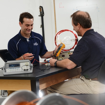 An engineering student and professor smile while working on a project on a lab table.