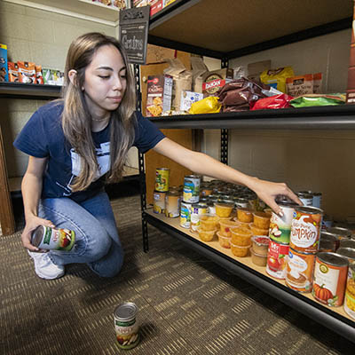 A student stocks cans of fruit on shelves.