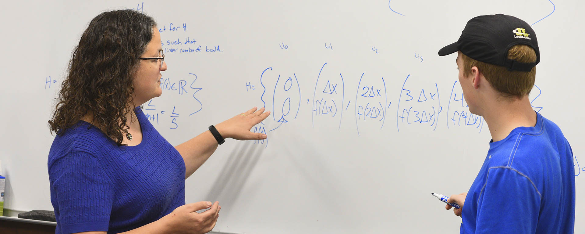 A math professor solves a problem with a student at the whiteboard.