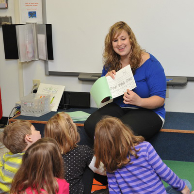 teacher smiling, reading to class with young students