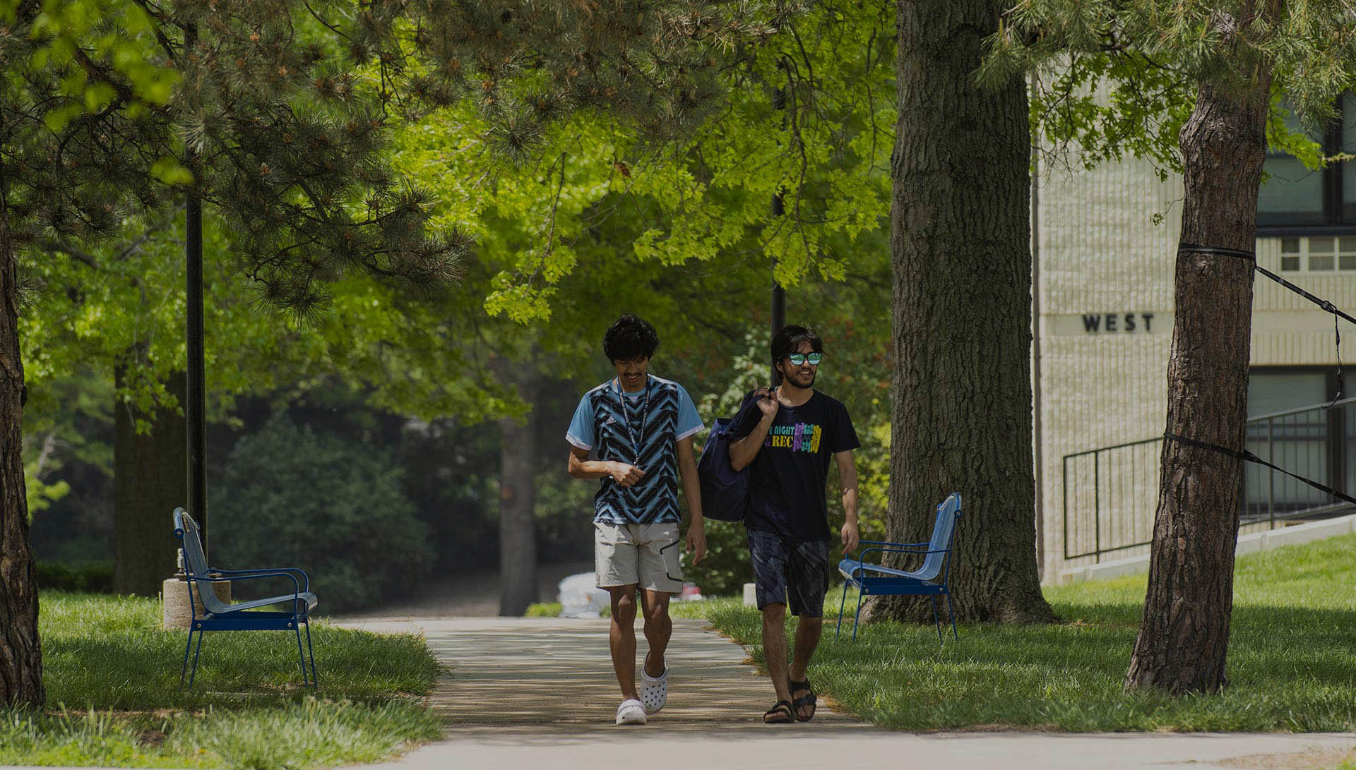Two students chat while walking on campus on a summer day.