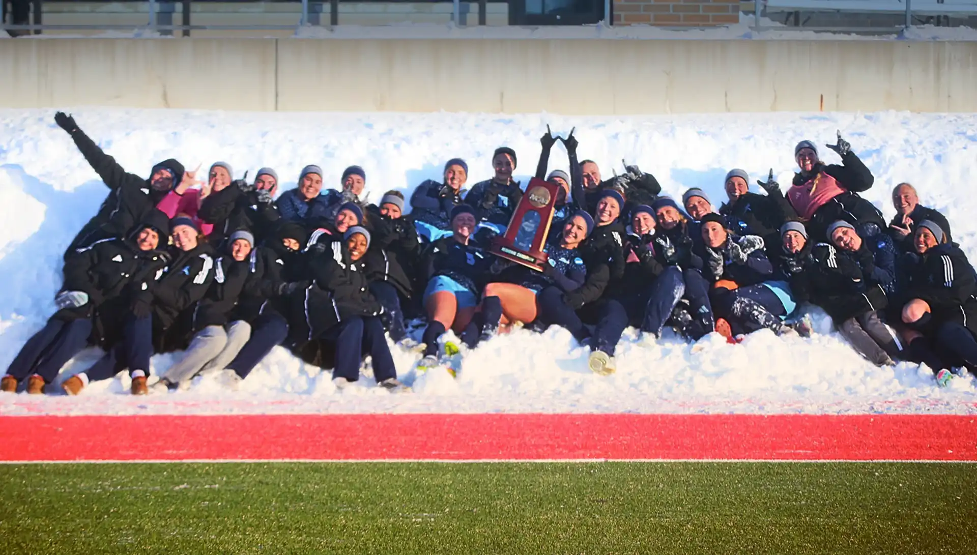 WU Women's Soccer group shot of team laying in snow, celebrating with trophy