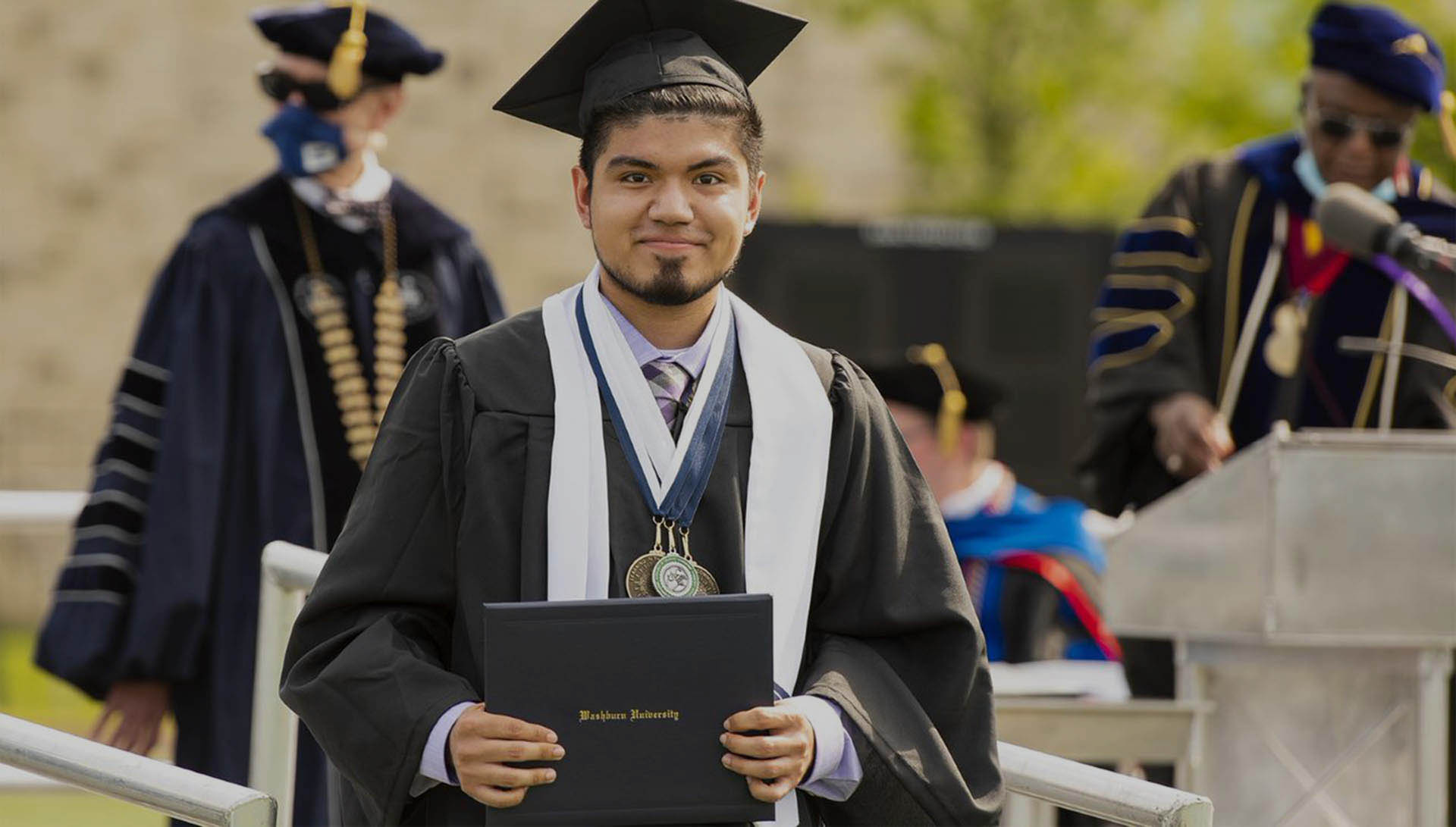 male student at commencement holding diploma