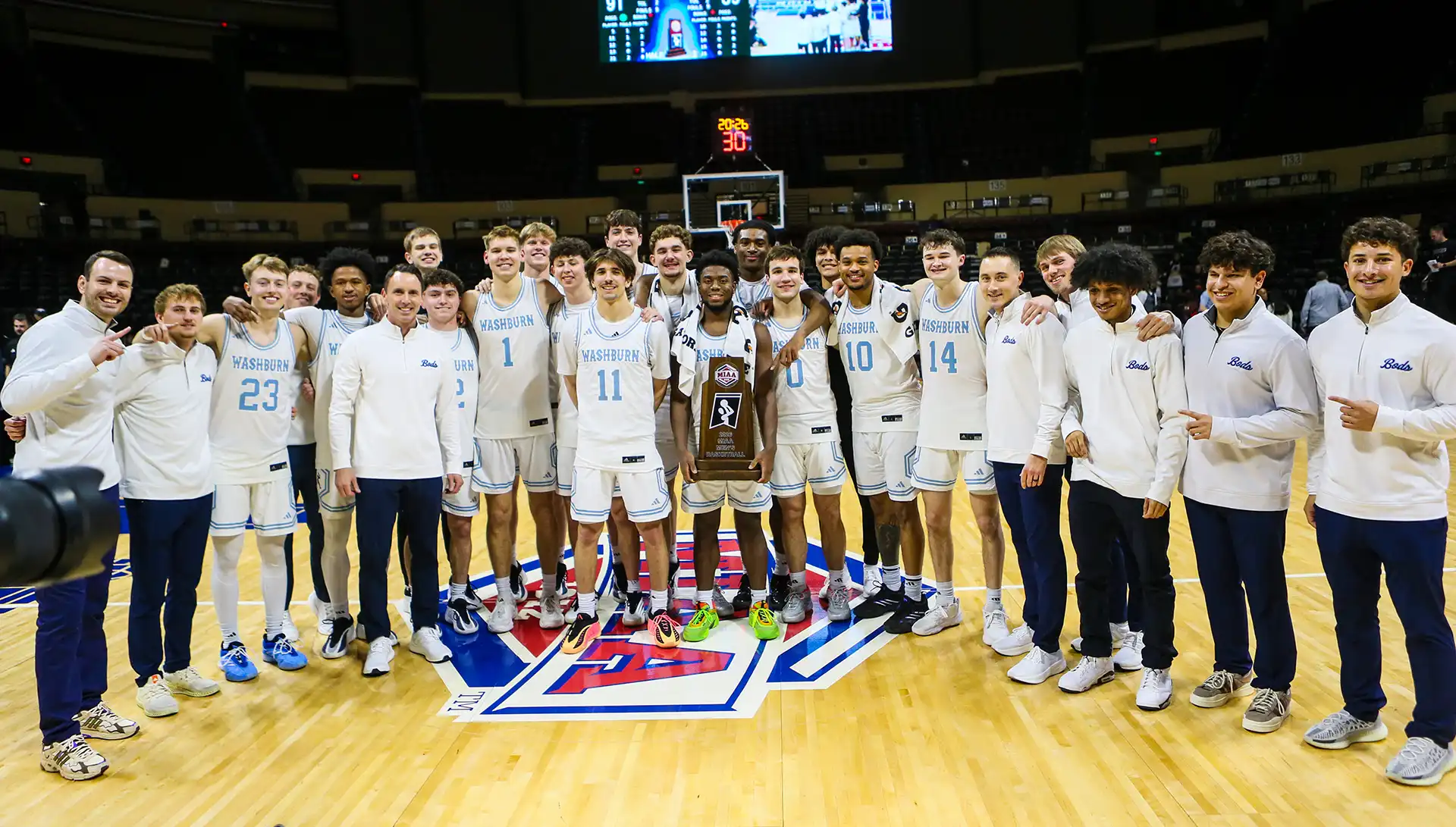 men's basketball team poses with trophy on court after championship win