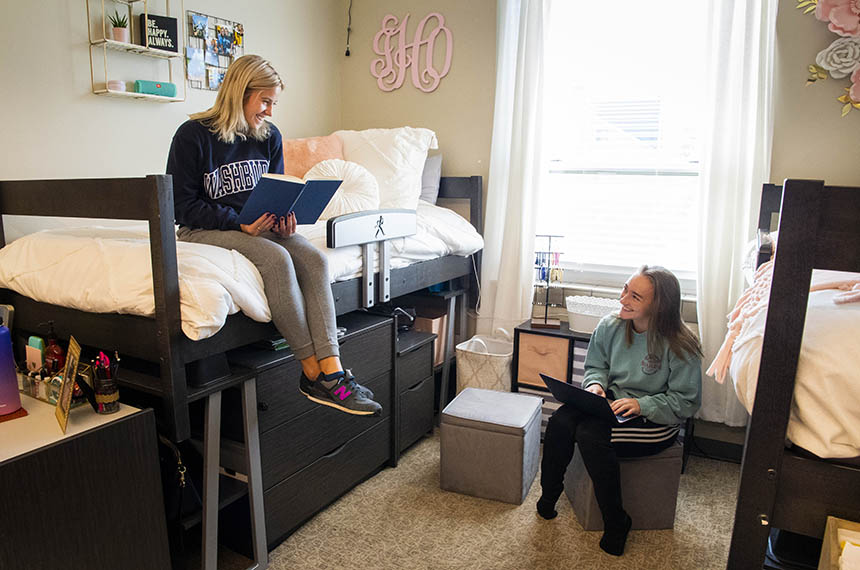 Two students smile while studying in their residence hall room.