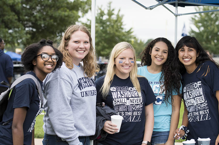 A group of students smile while tailgating at a football game.