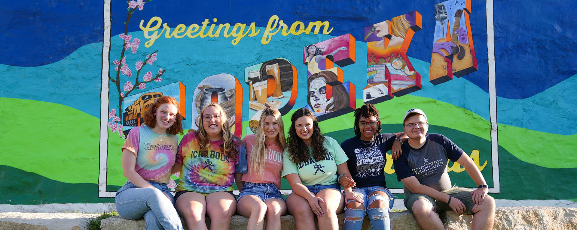 Washburn students smile for a photo in front of a "Greetings from Topeka" mural