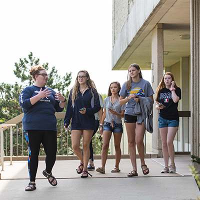 A student gestures while giving a tour outside to a group of new students