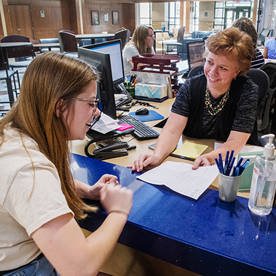 A staff member works with a student at the desk