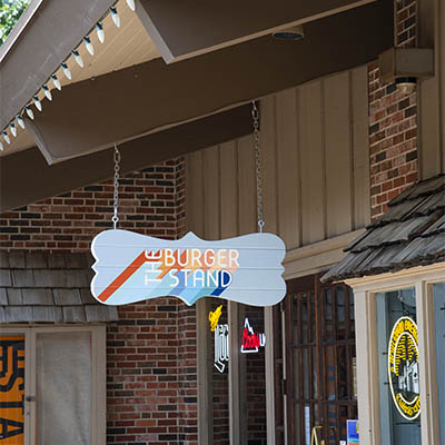 A colorful sign saying Burger Stand hangs from the rafters of a building.