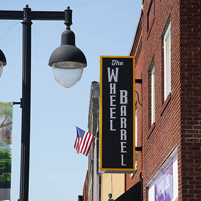 The Wheel Barrel sign hangs from a brick wall in the distance from a light post.