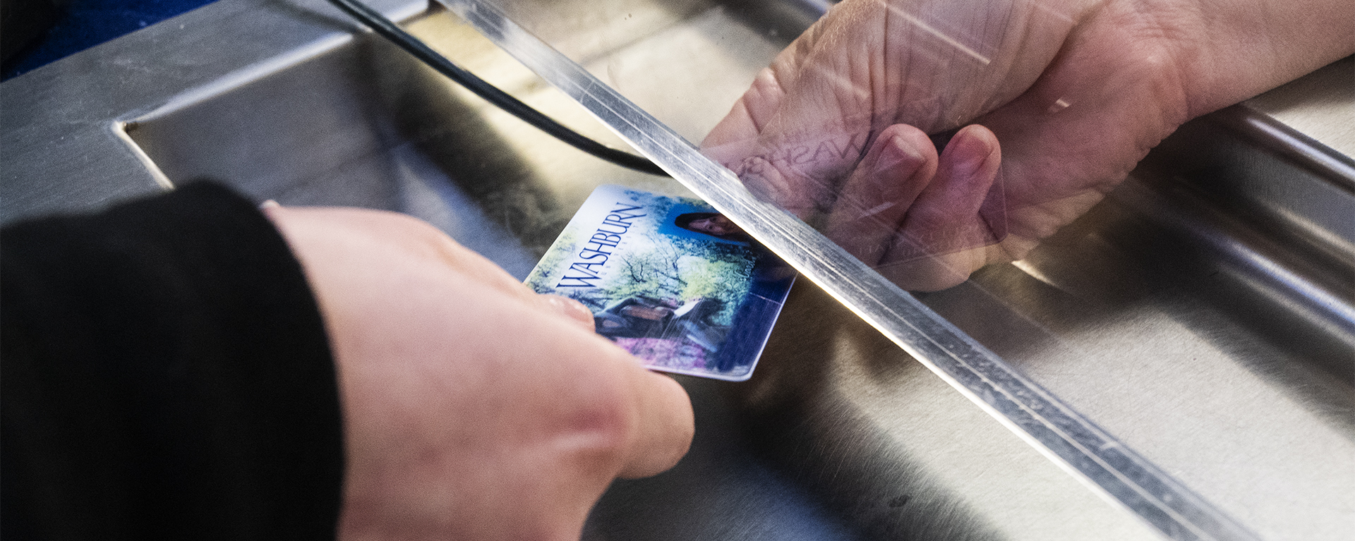 A Washburn ID is passed through the Business Office window in Morgan Hall.