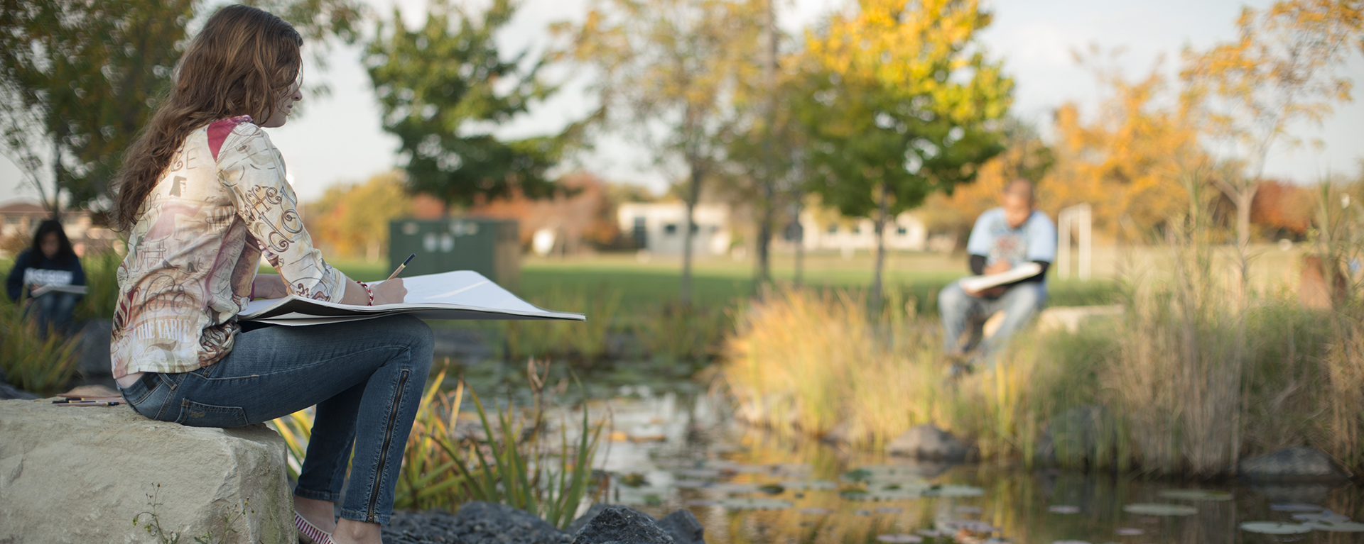 A Washburn student works on an art project by the Koi Pond on campus.