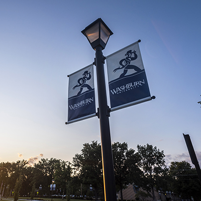 The sun sets behind Washburn flags on campus.