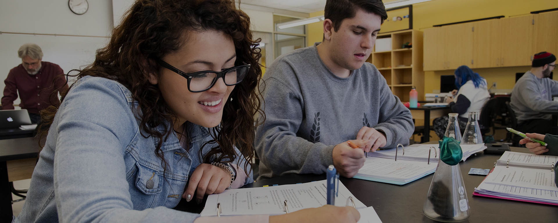 A student smiles while taking notes while in class.