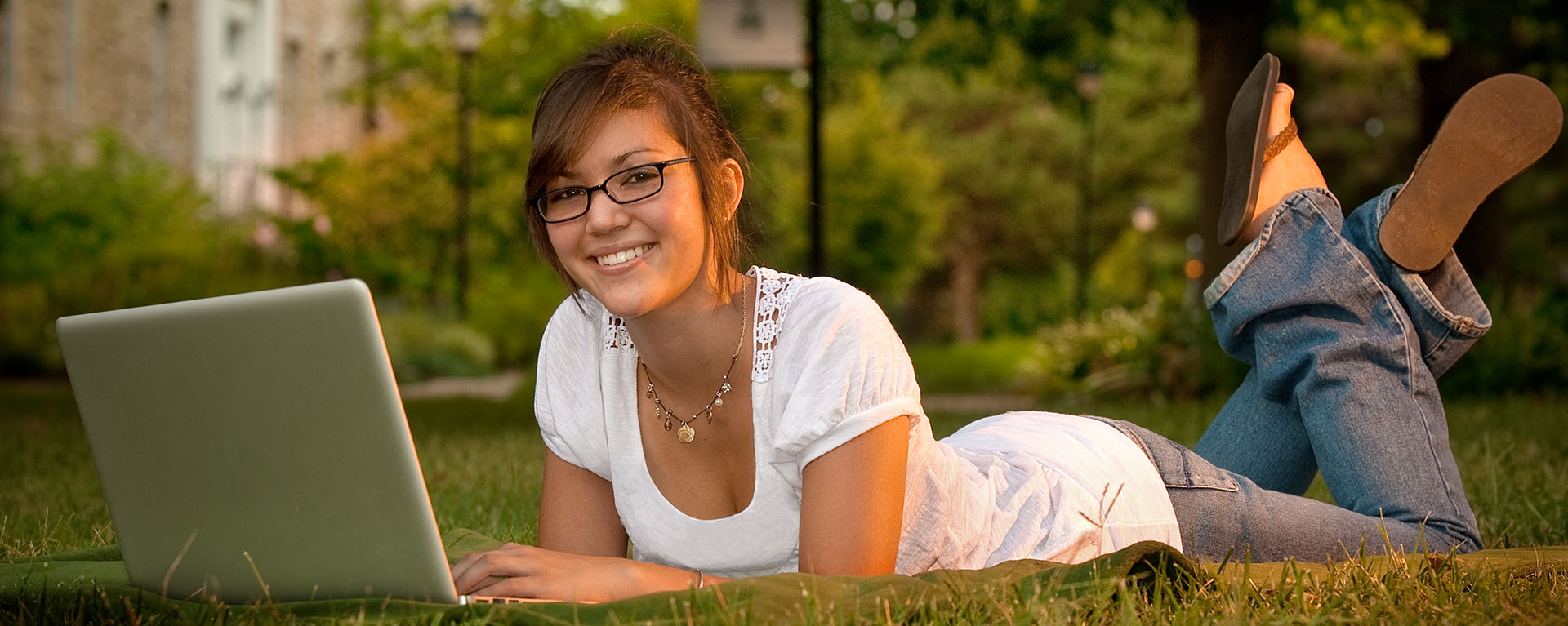 A Washburn student works on a laptop on the grass of the quad in the middle of campus.