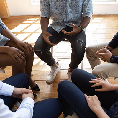 Overhead view of the hands of people sitting in a circle during a counseling session.