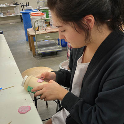 A student works with clay on a coffee cup.