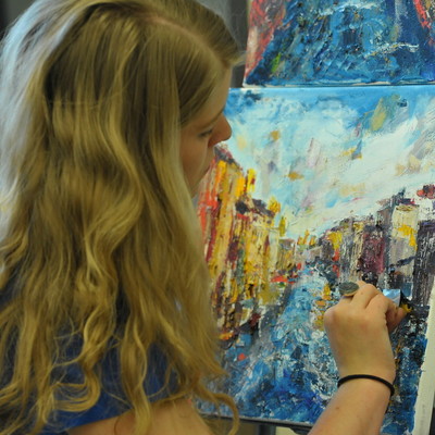 view from behind student painting on easel in classroom
