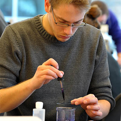 A student uses a pipette to add a sample to a slide.