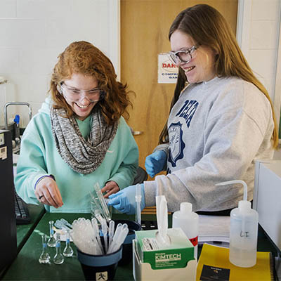 Two students work on an experiment while wearing safety goggles.