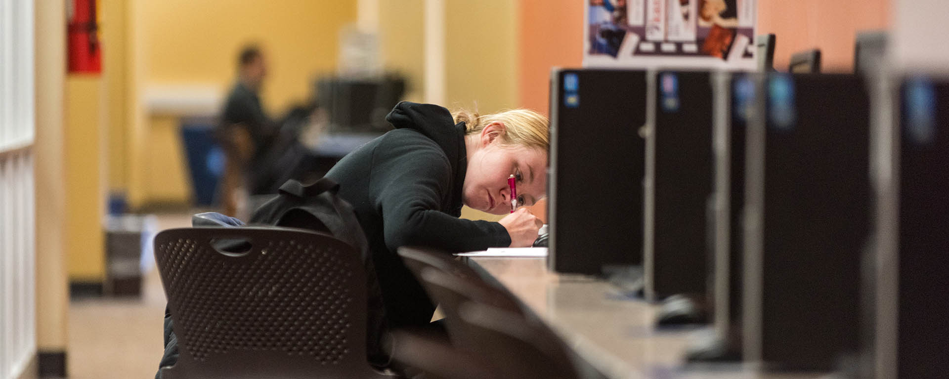 A student takes notes while at a computer in the library