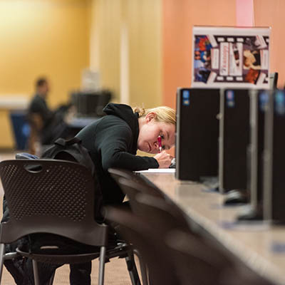 A student takes notes while sitting at a computer in the library