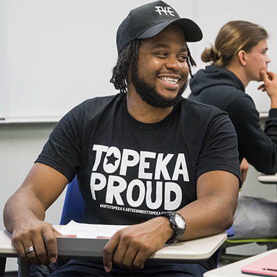 A student wearing a Topeka Proud shirt smiles while sitting in class.