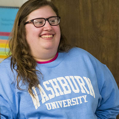 A student smiles while wearing a Washburn University sweatshirt in class.
