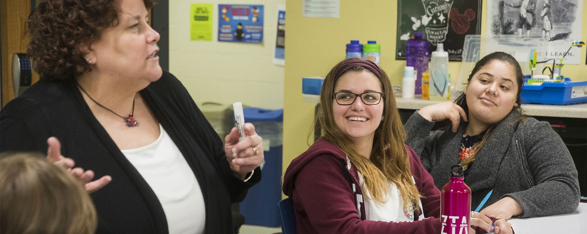 A student smiles while listening to a professor speak.