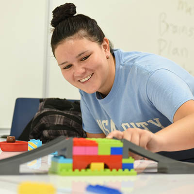 A student smiles while working with a toy car ramp in a classroom setting.