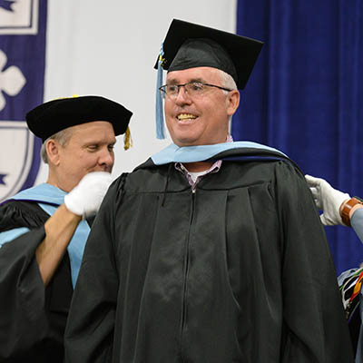 A graduate smiles while receiving their cape.