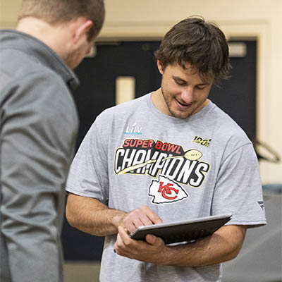 A student tests the reflexes of a student wearing a Washburn football shirt in a Kinesiology class.