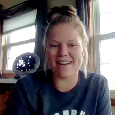 Katie smiles while talking to the camera while sitting in front of a window.