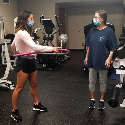 WU Moves student coach demonstrates an exercise with a weighted hoop around her waist for a client in the gym.