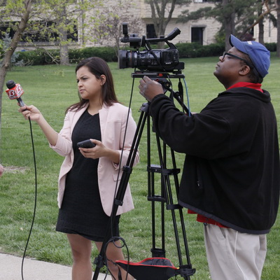 A tv journalist holds a microphone while her cameraman adjusts the shot.