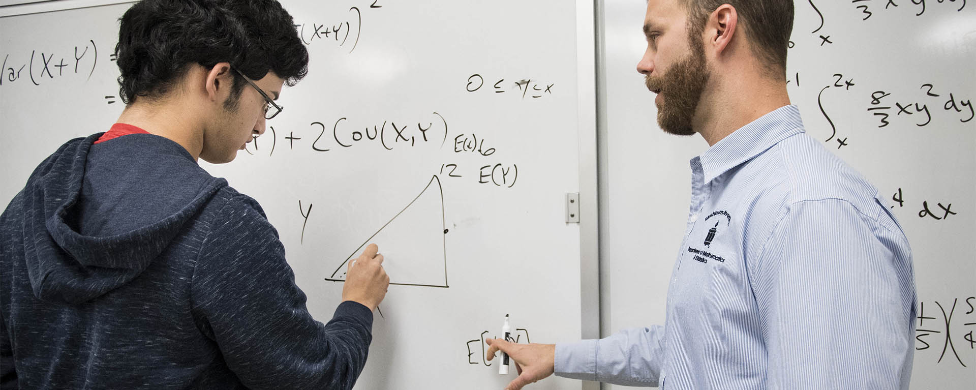 A student works a problem on the board with a professor