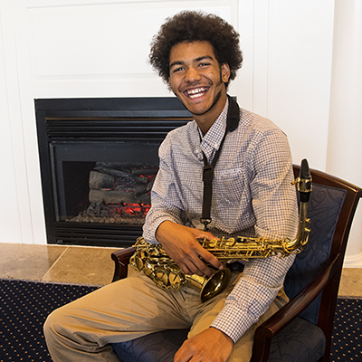 Music student, TyRese, sitting on a chair with a saxophone in his lap.
