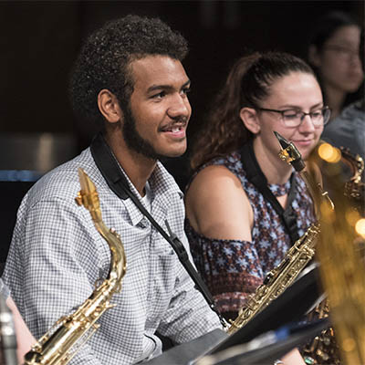 A music student smiles while holding a saxophone in a jazz band practice.