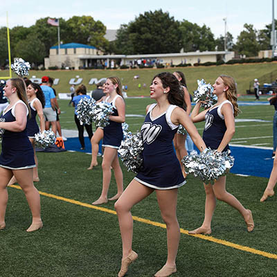 A group of dancing blues smile and cheer on football field