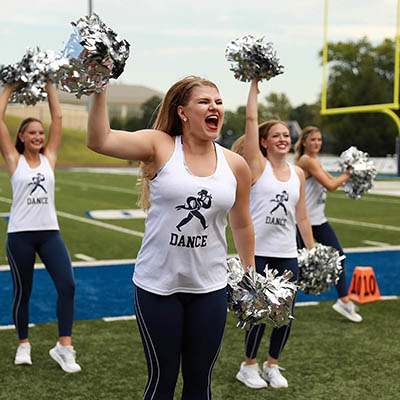 A dancer smiles and shouts cheers with other blues on football field