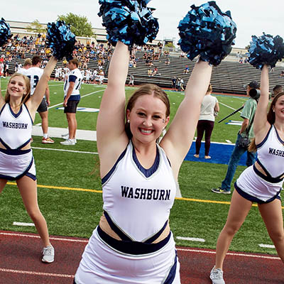 A dancing blue smiles and holds both poms in the air while cheering for the team.