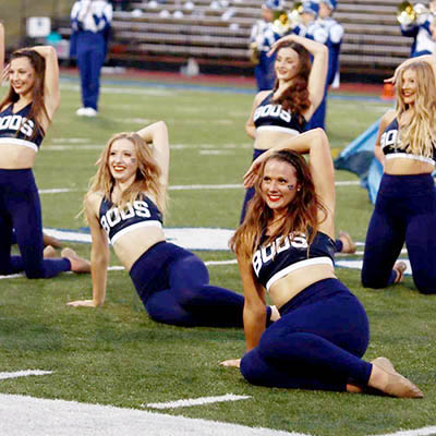 A dancer smiles while stretching out during a performance on the football field.