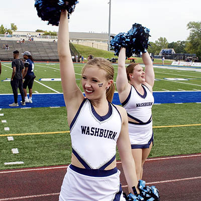 A dancer smiles and waves to the crowd during a football game.