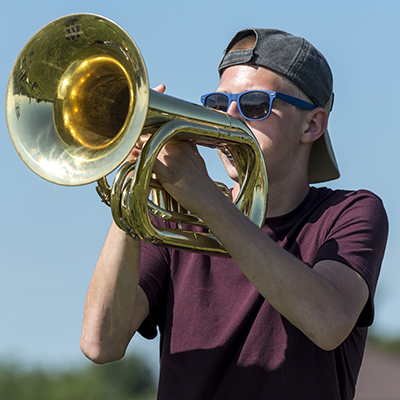 Student plays a horn outside for marching band practice.