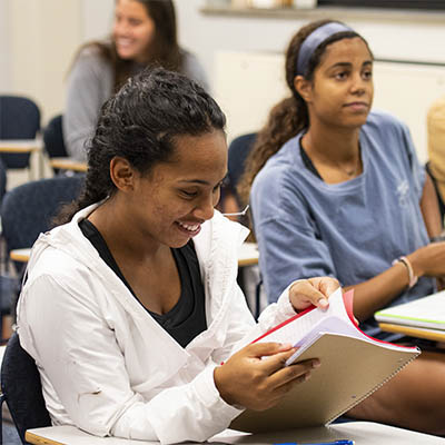 A student in a philosophy class smiles while looking through a book.