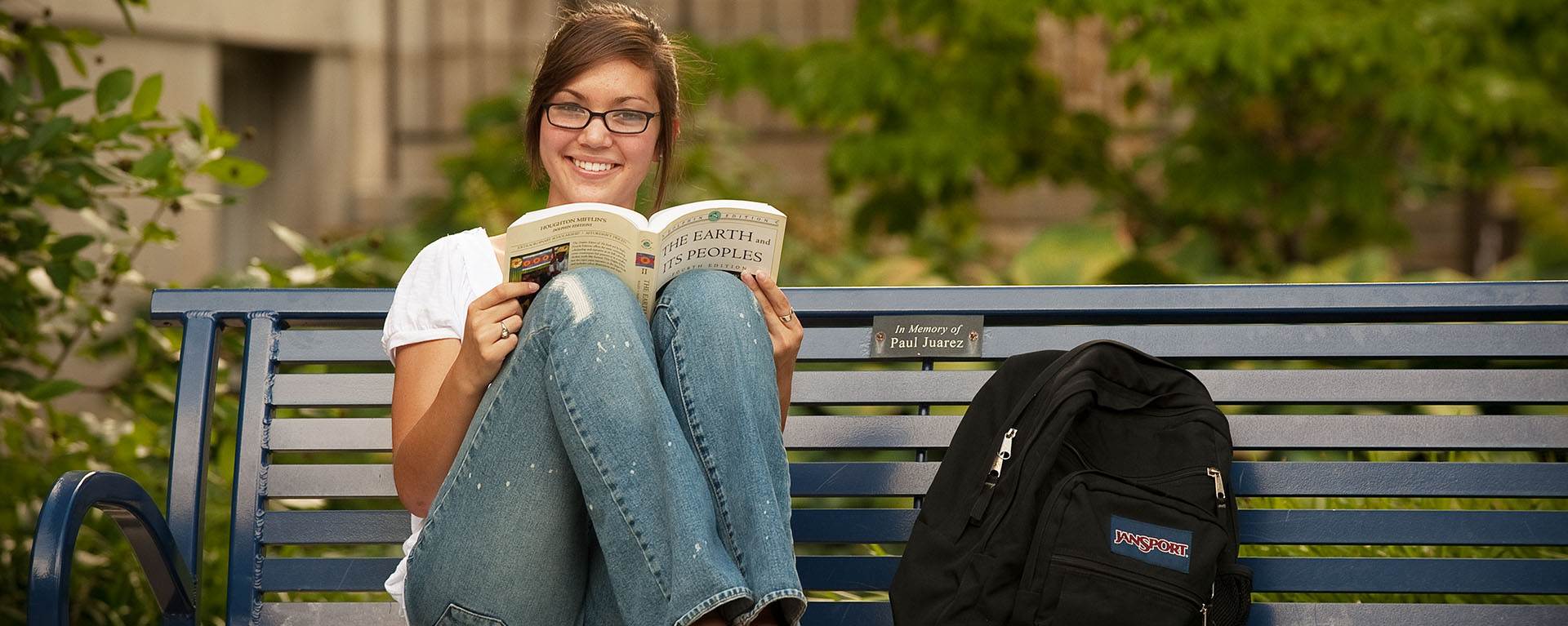 young woman sitting on bench reading
